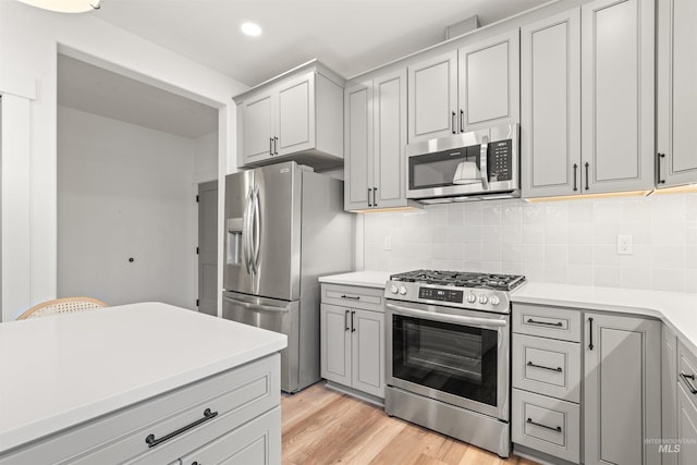 kitchen with decorative backsplash, light wood-type flooring, stainless steel appliances, and gray cabinetry