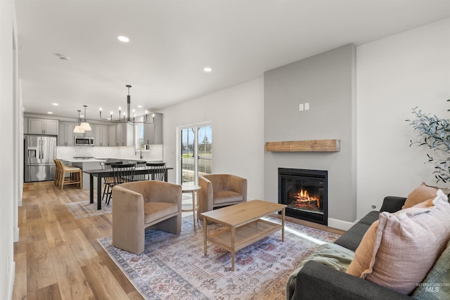 living room with sink, an inviting chandelier, and light wood-type flooring