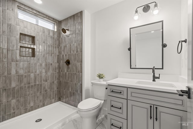 bathroom featuring a tile shower, vanity, and toilet