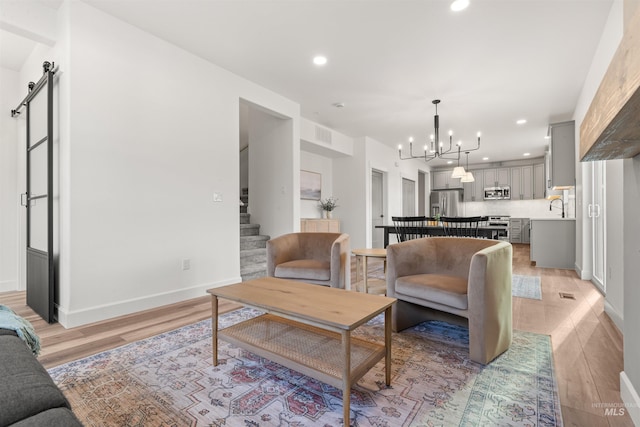 living room featuring a barn door, sink, a chandelier, and light hardwood / wood-style floors