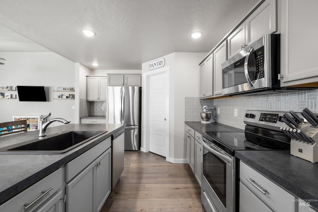 kitchen with stainless steel appliances, a sink, tasteful backsplash, dark wood-style flooring, and dark countertops