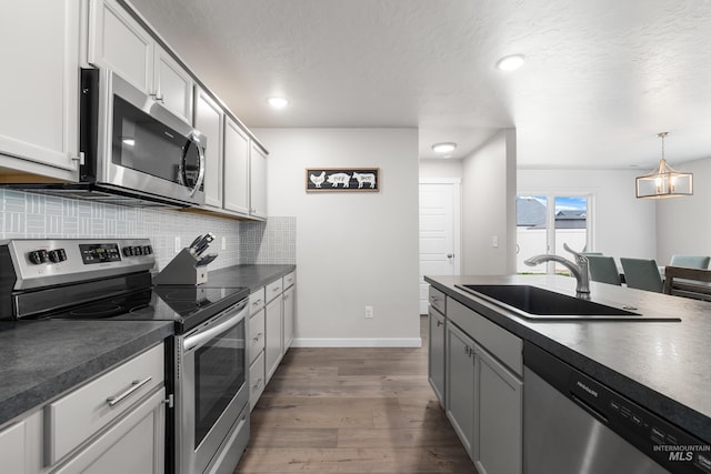 kitchen with a sink, dark wood-style flooring, dark countertops, decorative backsplash, and appliances with stainless steel finishes