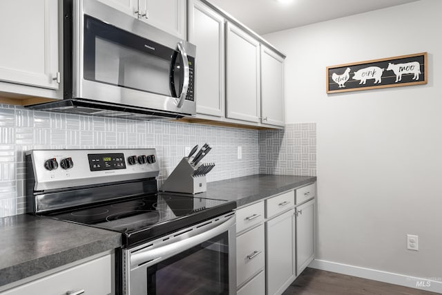 kitchen featuring dark countertops, tasteful backsplash, baseboards, appliances with stainless steel finishes, and dark wood-type flooring