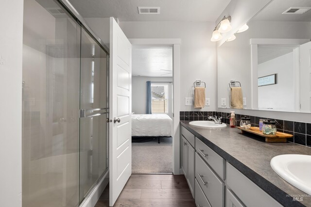bathroom featuring wood finished floors, a sink, a stall shower, double vanity, and visible vents