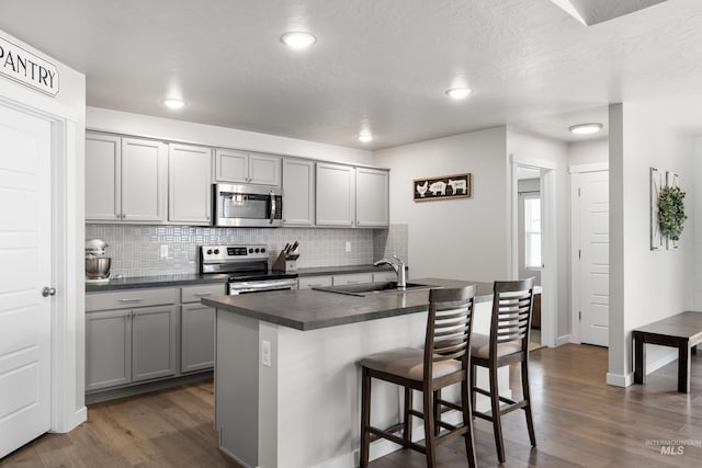 kitchen featuring dark countertops, a sink, gray cabinets, stainless steel appliances, and dark wood finished floors