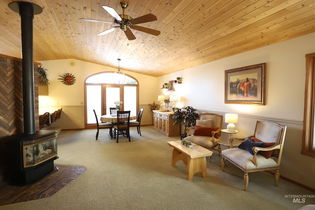 sitting room featuring lofted ceiling, wood ceiling, a wood stove, ceiling fan, and carpet