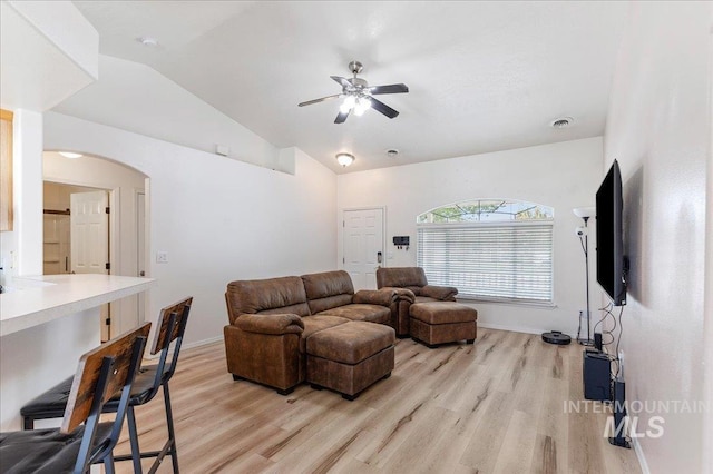 living room featuring arched walkways, a ceiling fan, vaulted ceiling, and light wood-type flooring
