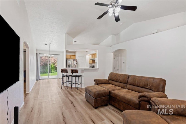 living area featuring arched walkways, ceiling fan, light wood-style flooring, and lofted ceiling