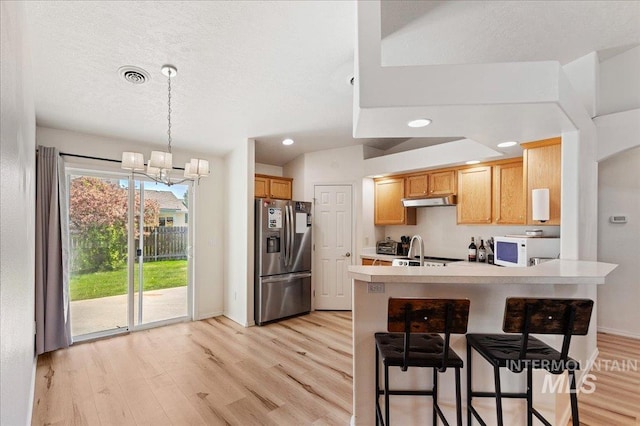 kitchen featuring a peninsula, white microwave, stainless steel fridge with ice dispenser, light wood finished floors, and a notable chandelier