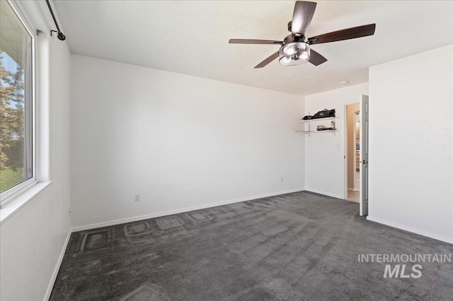 unfurnished room featuring a ceiling fan, baseboards, a healthy amount of sunlight, and dark carpet
