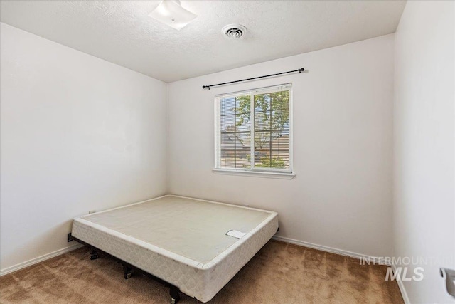 unfurnished bedroom with carpet floors, a textured ceiling, baseboards, and visible vents