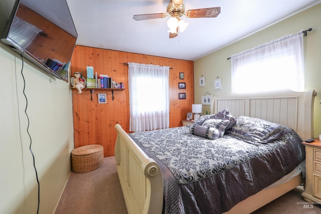 carpeted bedroom featuring ceiling fan and wooden walls