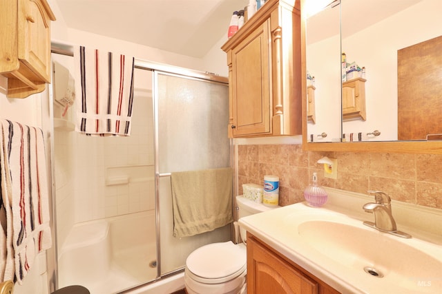 bathroom with toilet, vanity, decorative backsplash, and a shower with door