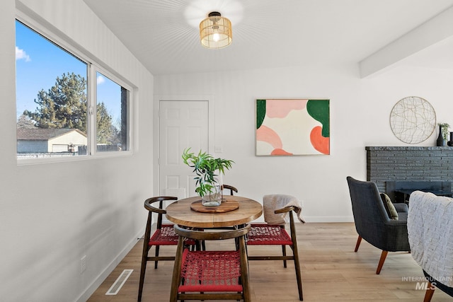 dining area featuring a fireplace, beam ceiling, and wood-type flooring