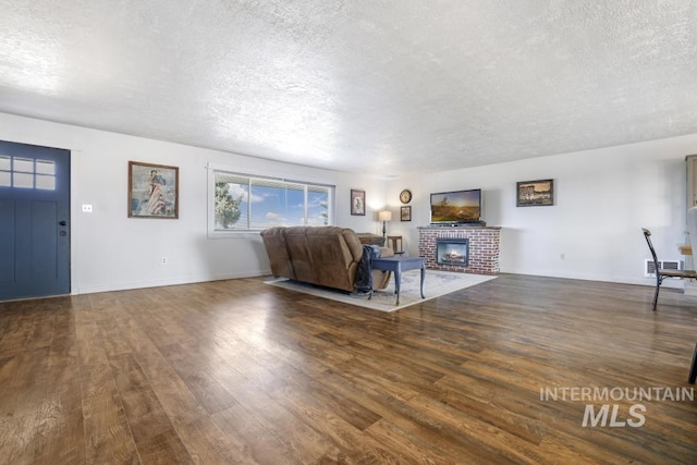 unfurnished living room with visible vents, a brick fireplace, a textured ceiling, and wood finished floors