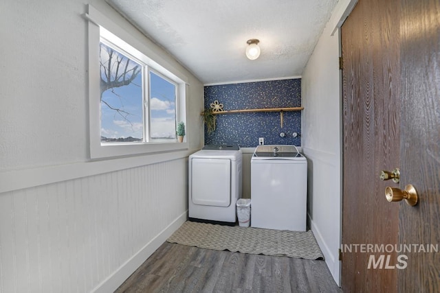 clothes washing area with wood finished floors, washing machine and dryer, wainscoting, wallpapered walls, and laundry area