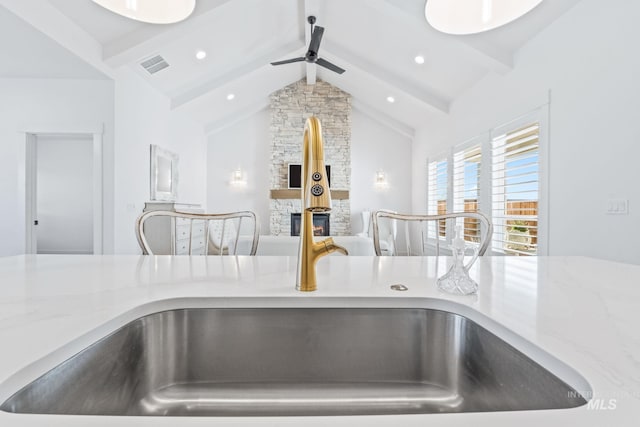 8456 W Meltwater Ln, Eagle, ID 83616 - kitchen view of beamed ceiling, ceiling fan, light stone countertops, a sink, and a fireplace