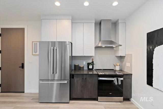 kitchen featuring dark countertops, modern cabinets, wall chimney range hood, white cabinets, and appliances with stainless steel finishes
