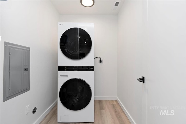 laundry area featuring laundry area, baseboards, light wood-style floors, electric panel, and stacked washer / drying machine