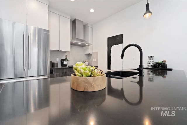 kitchen with decorative backsplash, a sink, white cabinets, freestanding refrigerator, and wall chimney exhaust hood