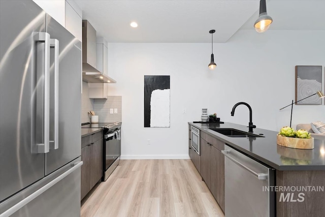kitchen with a sink, dark countertops, stainless steel appliances, and wall chimney exhaust hood