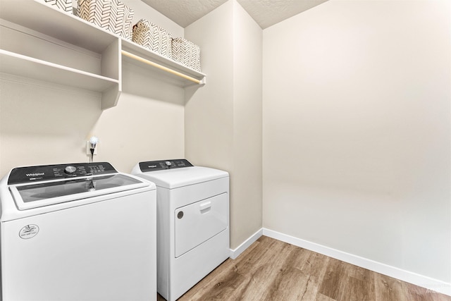 clothes washing area featuring washing machine and dryer, light hardwood / wood-style flooring, and a textured ceiling