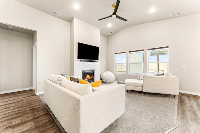 living room with hardwood / wood-style floors, vaulted ceiling, ceiling fan, and a tiled fireplace