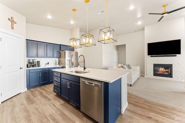 kitchen with blue cabinetry, an island with sink, decorative light fixtures, a fireplace, and appliances with stainless steel finishes