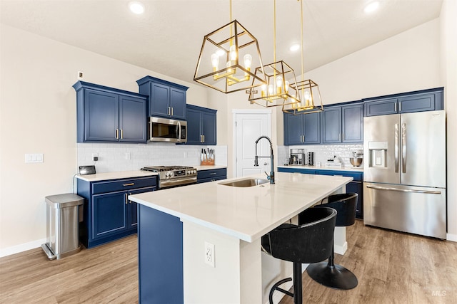 kitchen with blue cabinetry, sink, stainless steel appliances, pendant lighting, and a kitchen island with sink