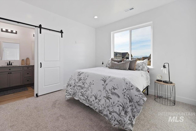 bedroom with visible vents, baseboards, a barn door, ensuite bathroom, and a sink