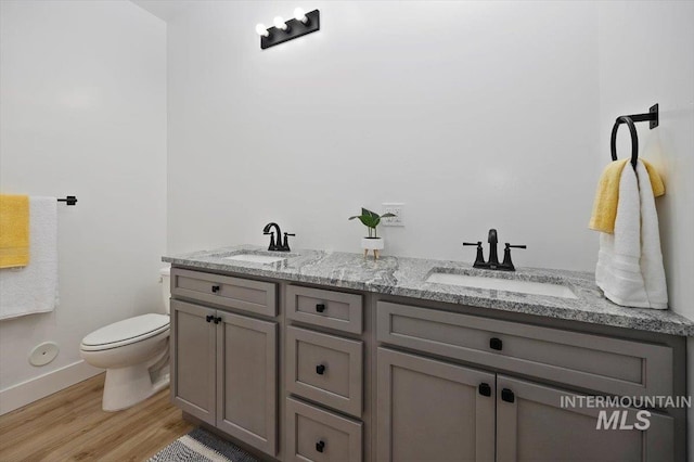 bathroom featuring wood finished floors, baseboards, double vanity, a sink, and toilet