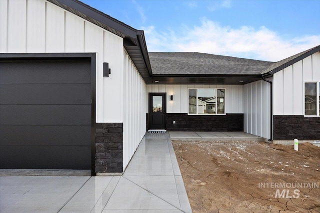 doorway to property with a garage, stone siding, roof with shingles, and board and batten siding