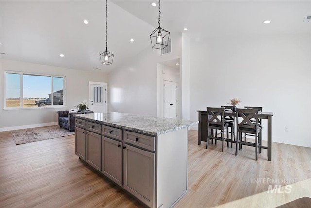 kitchen featuring light stone counters, gray cabinetry, light wood-style floors, pendant lighting, and a center island