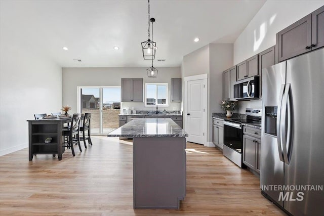 kitchen featuring a center island, light wood-style flooring, appliances with stainless steel finishes, stone countertops, and a sink