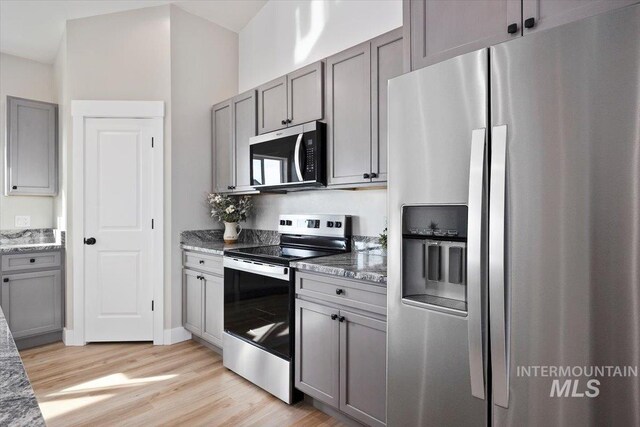 kitchen featuring light stone counters, gray cabinetry, light wood finished floors, and stainless steel appliances