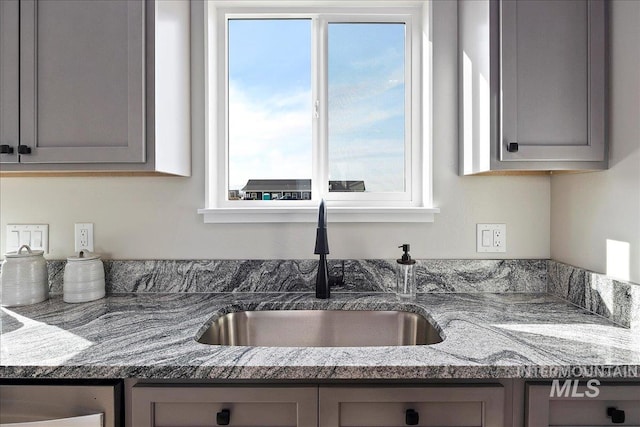 kitchen with a sink, light stone countertops, and gray cabinetry