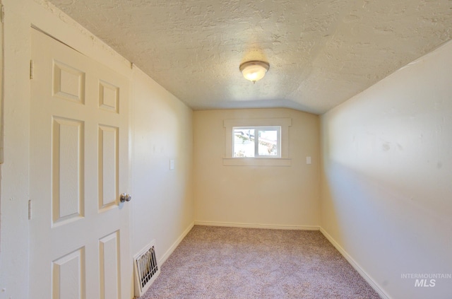 spare room featuring carpet, baseboards, visible vents, lofted ceiling, and a textured ceiling