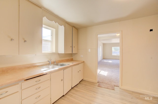 kitchen featuring baseboards, a sink, light countertops, light wood-style floors, and cream cabinets