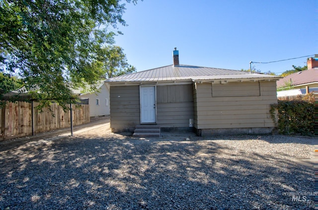 rear view of property with a chimney, entry steps, metal roof, and fence