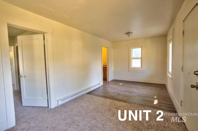 empty room with a baseboard radiator, carpet floors, baseboards, and wood finished floors