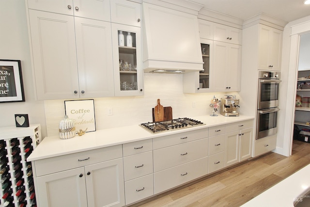 520 S Prospector Ln, Eagle, ID 83616 - kitchen featuring stainless steel appliances, premium range hood, decorative backsplash, light wood-type flooring, and light countertops