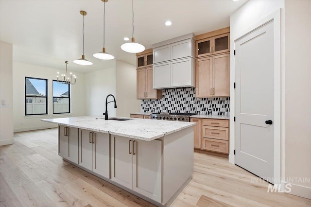 kitchen with light hardwood / wood-style floors, sink, a kitchen island with sink, a notable chandelier, and light stone counters