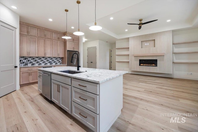 kitchen with light stone countertops, pendant lighting, dishwasher, sink, and a center island with sink