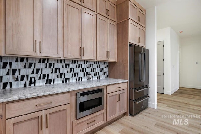 kitchen with tasteful backsplash, light wood-type flooring, appliances with stainless steel finishes, light brown cabinets, and light stone counters