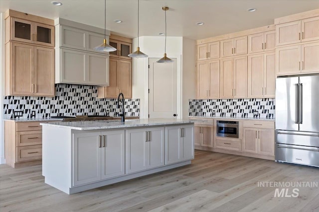 kitchen featuring light stone countertops, pendant lighting, appliances with stainless steel finishes, and an island with sink