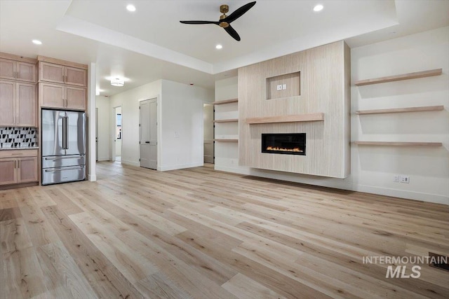 unfurnished living room featuring ceiling fan, a tray ceiling, and light hardwood / wood-style floors