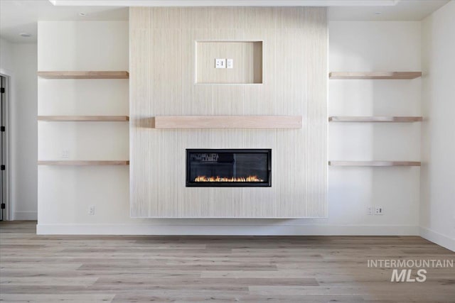 unfurnished living room with light wood-type flooring, a large fireplace, and built in shelves