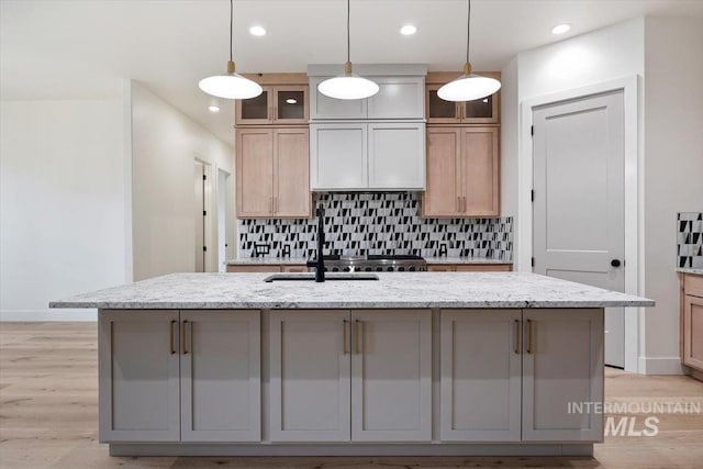 kitchen featuring light stone countertops, hanging light fixtures, a kitchen island with sink, and tasteful backsplash