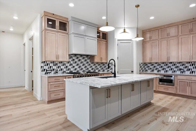 kitchen with light stone countertops, stainless steel appliances, light hardwood / wood-style floors, sink, and a center island with sink