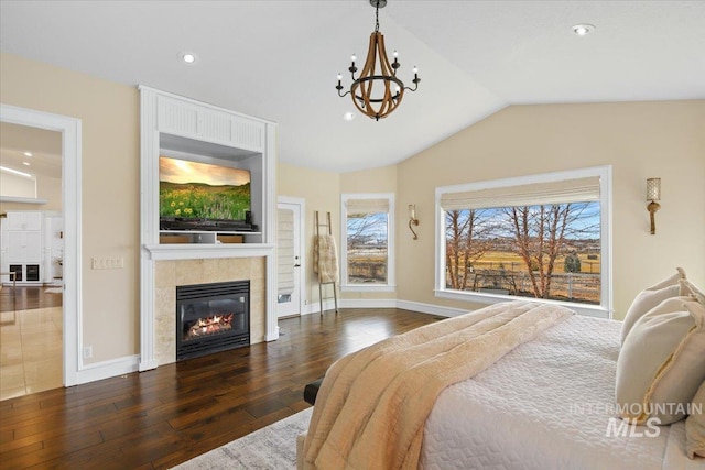 bedroom featuring dark hardwood / wood-style floors, a chandelier, vaulted ceiling, and a tile fireplace